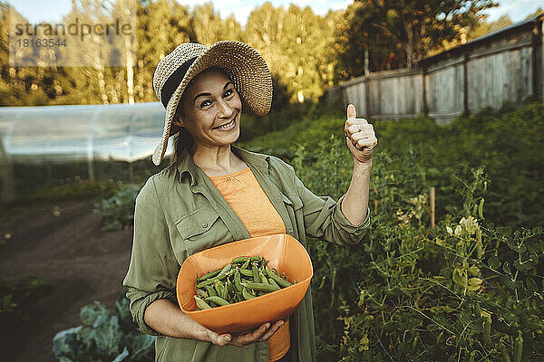 Lächelnde Frau mit einer Schüssel grüner Erbsen gestikuliert im Garten
