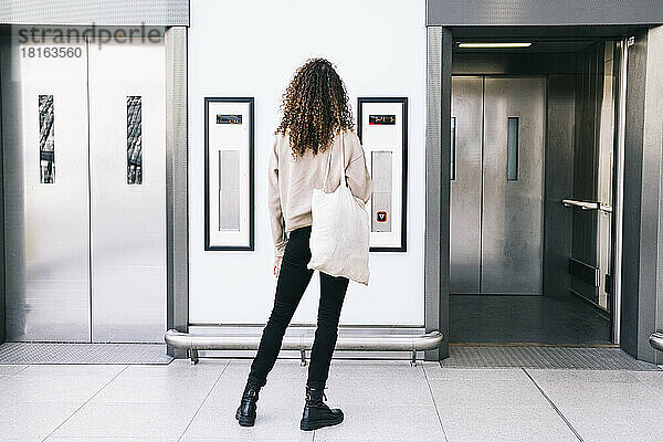 Frau mit lockigem Haar steht vor dem Aufzug