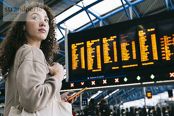 Junge Frau mit Mobiltelefon steht vor der Zeittafel