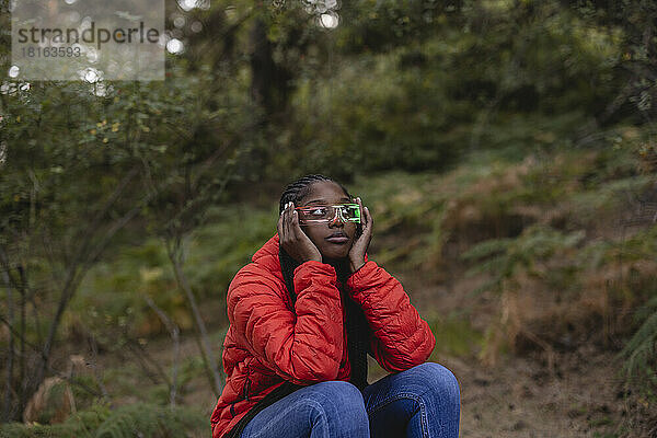 Junge Frau mit futuristischer Brille sitzt im Wald