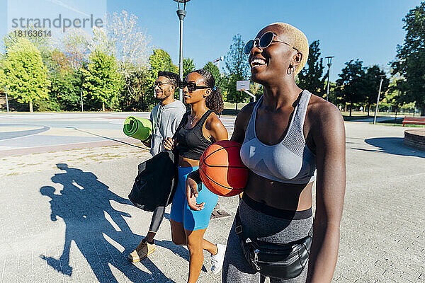 Lächelnde Sportlerin mit Basketball läuft an Freunden auf dem Fußweg vorbei