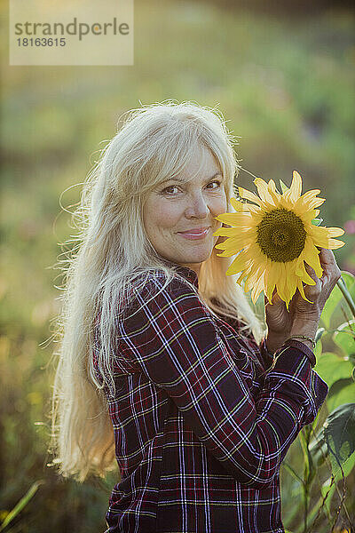 Lächelnde reife Frau hält an einem sonnigen Tag eine Sonnenblume