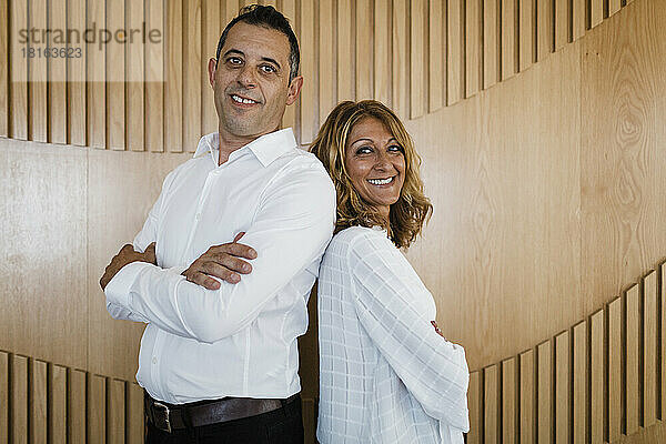 Happy business colleagues with arms crossed standing in front of wall