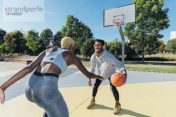 Smiling sportsman playing basketball with friend in sports court