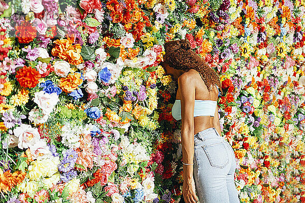 Young curly hair woman leaning head on flower wall