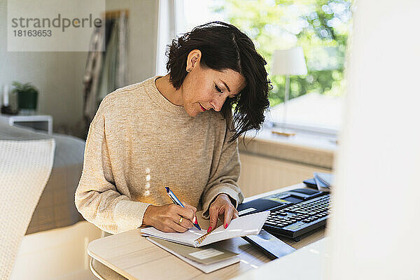 Reife Geschäftsfrau schreibt zu Hause in Notizblock auf dem Tisch