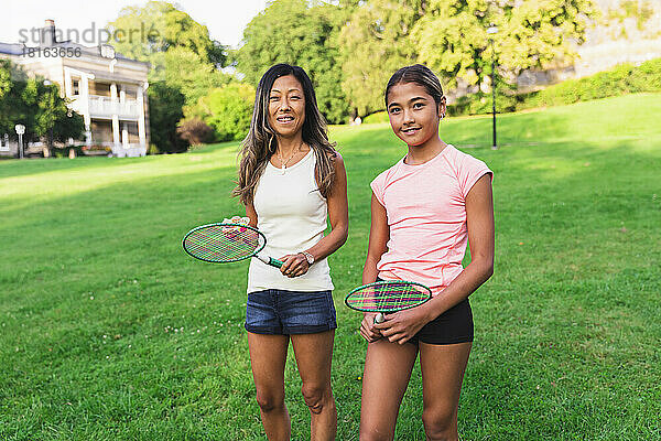 Mutter und Tochter mit Badmintonschläger stehen auf Gras im Rasen