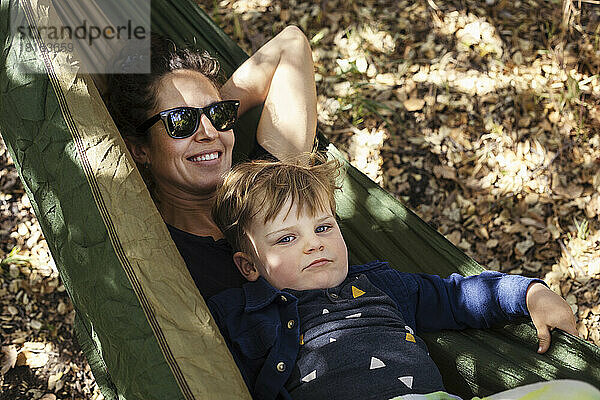 Lächelnde Frau mit Sohn  der sich in der Hängematte entspannt
