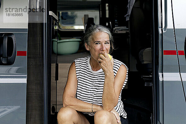 Ältere Frau isst Apfel am Eingang eines Wohnmobils