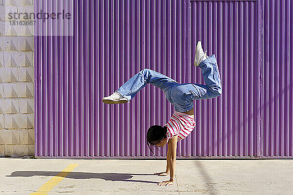 Young woman doing handstand in front of corrugated wall