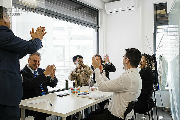Fröhliche Geschäftskollegen applaudieren gemeinsam bei einem Treffen im Büro