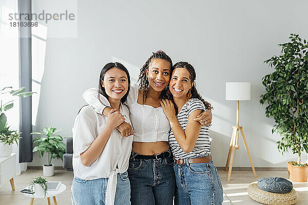 Happy multiracial friends with arms around in living room