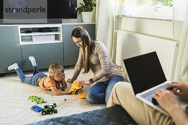 Mutter und Sohn spielen mit Spielzeug  während der Vater zu Hause auf dem Sofa arbeitet