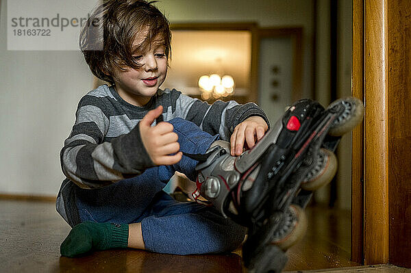 Cute boy wearing roller skates sitting on floor at home