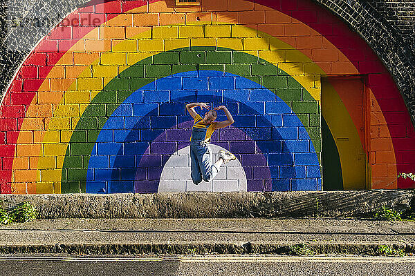 Fröhliche Transgender-Person springt vor Regenbogenwand