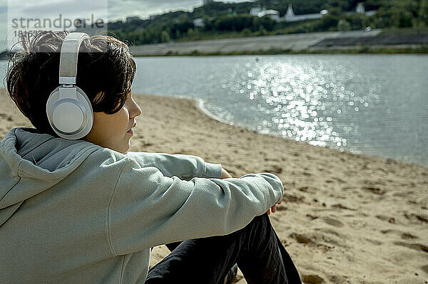 Junge trägt kabellose Kopfhörer und hört am Strand Musik