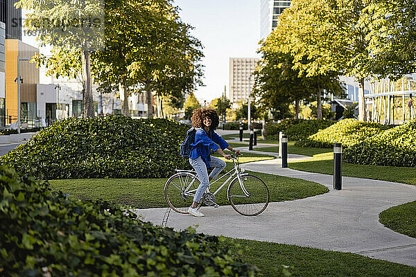 Lächelnde Frau mit Fahrrad auf Fußweg im Park
