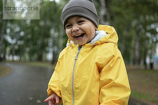 Netter glücklicher Junge mit Strickmütze und gelber Regenjacke