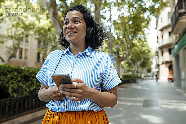 Lächelnde Frau genießt Musik über Kopfhörer auf dem Fußweg