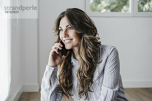 Lächelnde Geschäftsfrau im Büro mit Mobiltelefon am Fenster