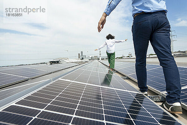 Geschäftsfrau und Geschäftsmann gehen zwischen Sonnenkollektoren auf dem Dach spazieren