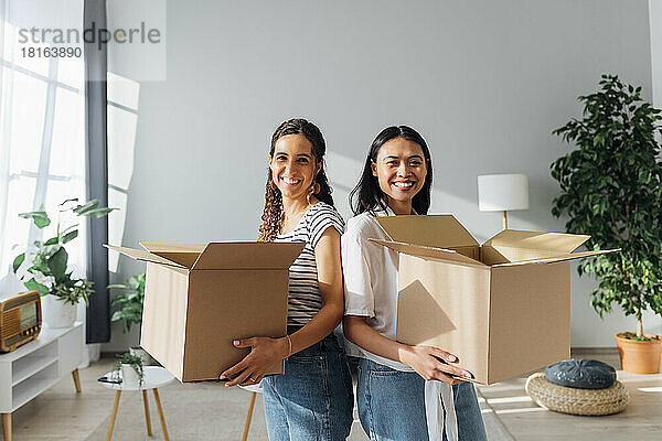 Smiling friends with cardboard boxes moving in new house