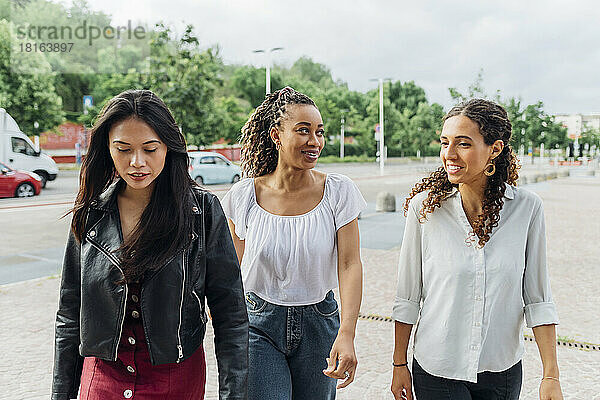 Smiling multiracial friends walking on footpath