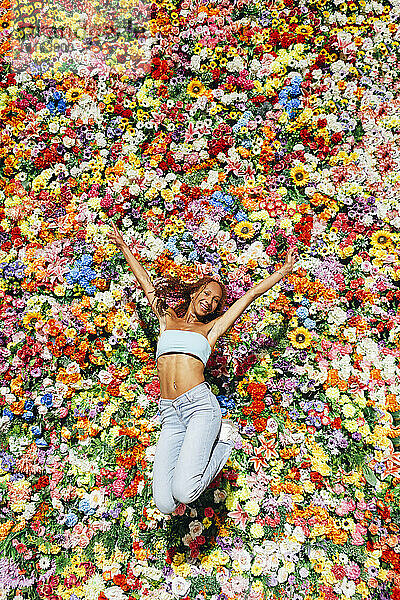 Happy young woman jumping in front of multi colored flower wall