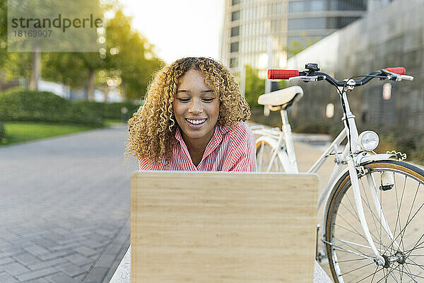 Glückliche Frau bei Videoanruf über Laptop mit dem Fahrrad