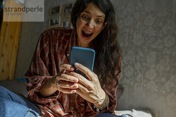 Überraschte Frau  die zu Hause ihr Mobiltelefon benutzt