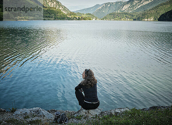 Reife Frau sitzt auf einem Felsen am Seeufer