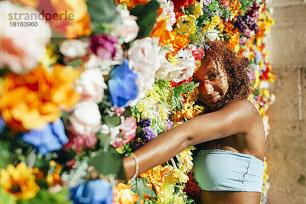 Lächelnde junge Frau lehnt an einer bunten Blumenwand