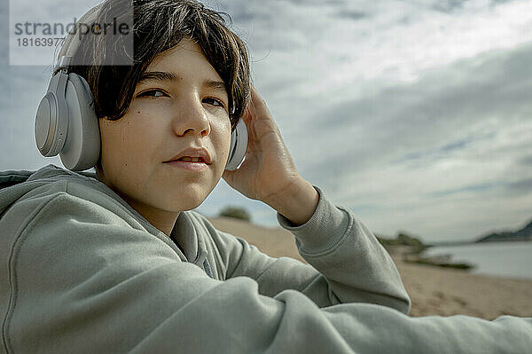 Junge mit kabellosen Kopfhörern sitzt unter bewölktem Himmel