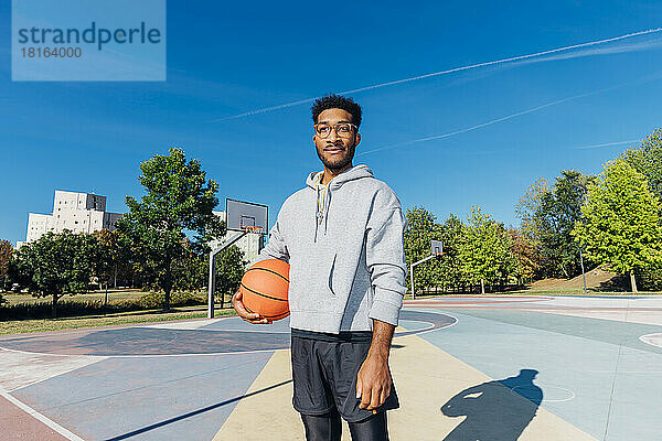 Selbstbewusster Spieler mit Basketballball im Spielfeld an einem sonnigen Tag