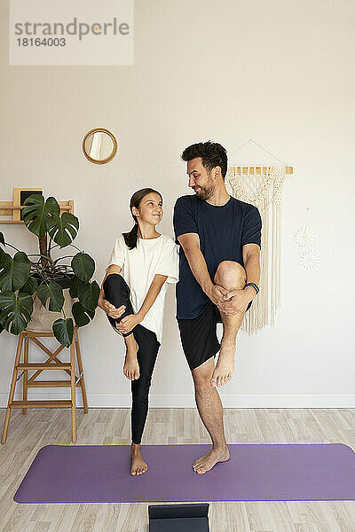 Lächelndes Mädchen mit Vater beim Yoga auf der Gymnastikmatte zu Hause