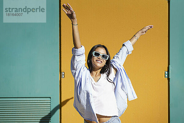 Glückliche junge Frau mit Sonnenbrille  die an einem sonnigen Tag Spaß vor der Wand hat