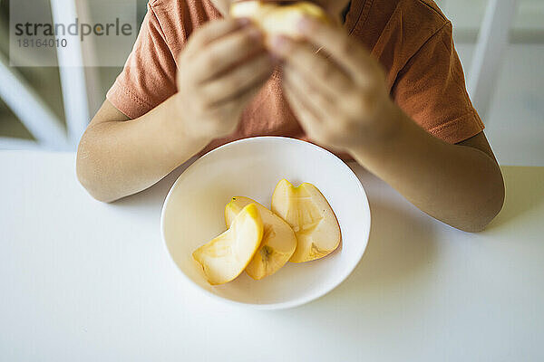 Slices of apple in bowl on table by boy at home