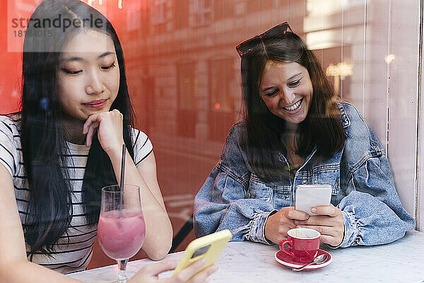 Frau mit Hand am Kinn benutzt Smartphone von lesbischer Freundin im Café