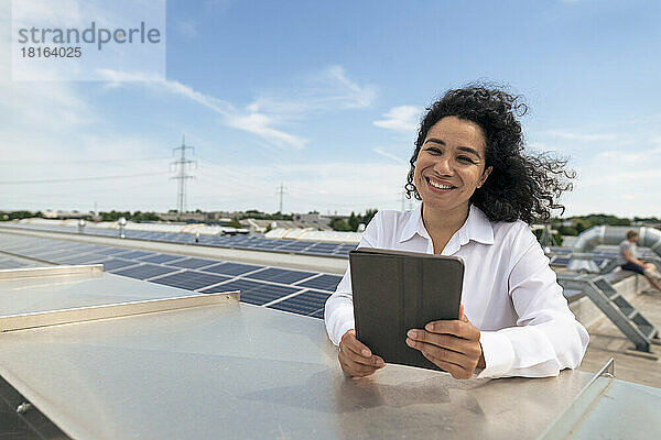 Glückliche Geschäftsfrau hält Tablet-PC vor Sonnenkollektoren