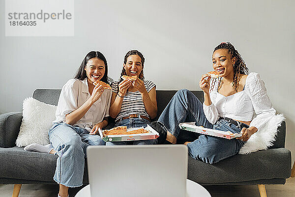 Glückliche Mitbewohner  die zu Hause auf dem Sofa einen Film schauen und Pizza essen