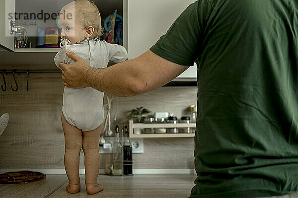 Baby girl standing on kitchen counter with father at home