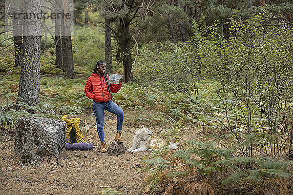 Junge Frau liest Karte mit Hund  der im Wald sitzt