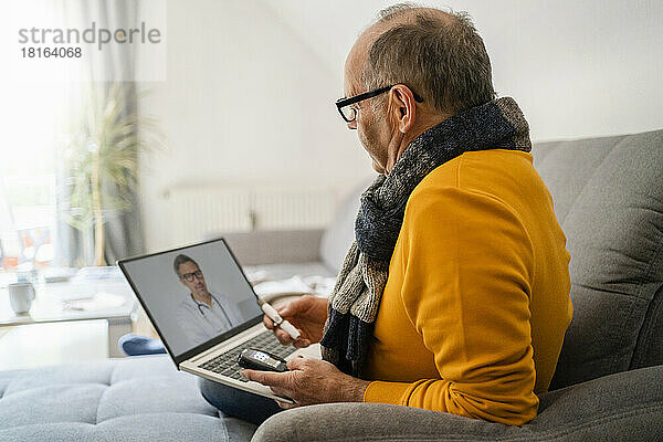 Mann führt Online-Konsultation mit Arzt über Laptop auf Sofa zu Hause durch