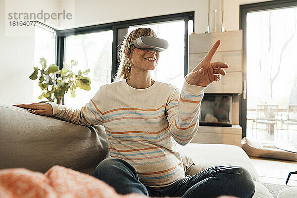 Werdende Frau mit Virtual-Reality-Headset gestikuliert zu Hause