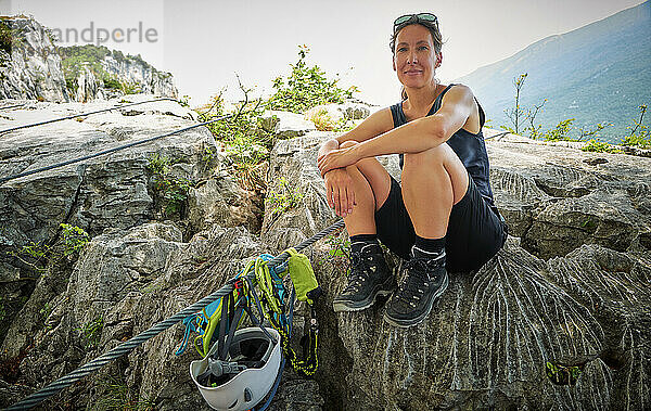 Frau sitzt neben Kletterausrüstung auf Felsen