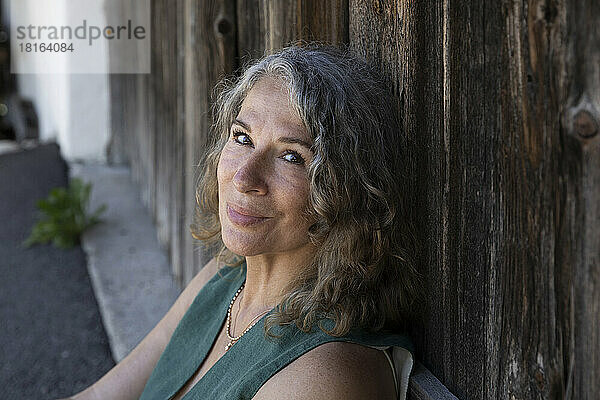 Lächelnde grauhaarige Frau lehnt an einer Holztür