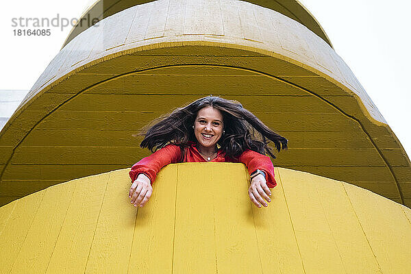 Glückliche junge Frau schaut aus gelbem Gebäude