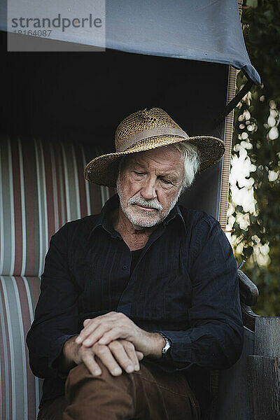 Trauriger älterer Mann mit Hut sitzt auf dem Bauernhof