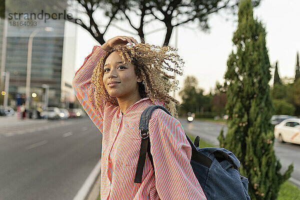 Young woman with curly blond hair carrying backpack crossing street