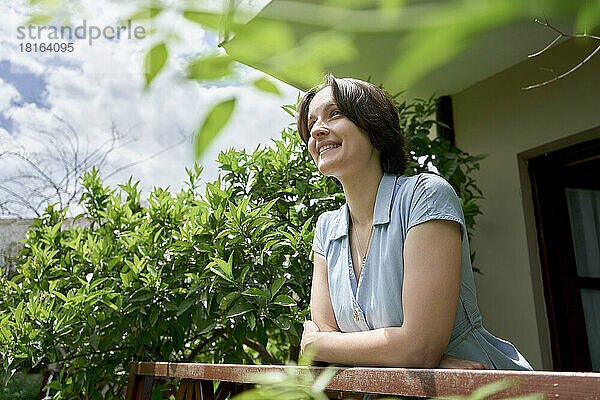 Lächelnde Frau steht an einem sonnigen Tag auf dem Balkon